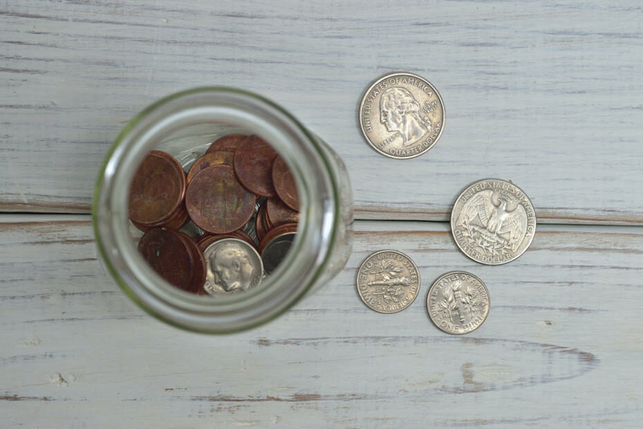 Looking directly down a table, there's a tip jar with coins inside and four coins spread out on the table next to the jar. Many online crowdfunding platforms work like this tip jar.