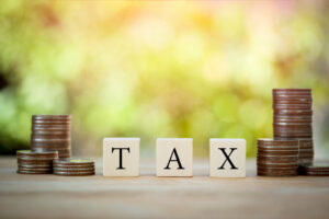 Three stacks of coins of unequal height each on the left and right of three blocks that spell out TAX, used to illustrate our tax guide for small businesses